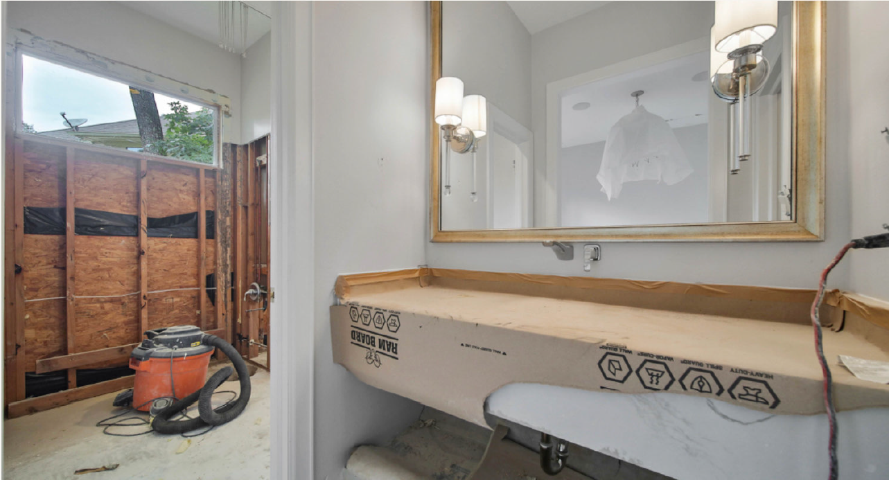 Small bathroom with sink and mirror beside a shower under renovation; vacuum sits on the floor.