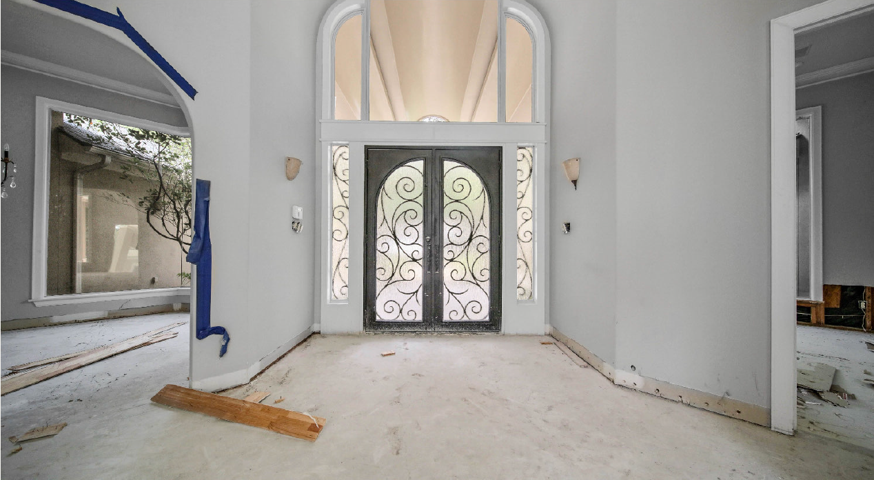 Empty foyer with ornate glass double doors, white walls, and a broom on the floor.