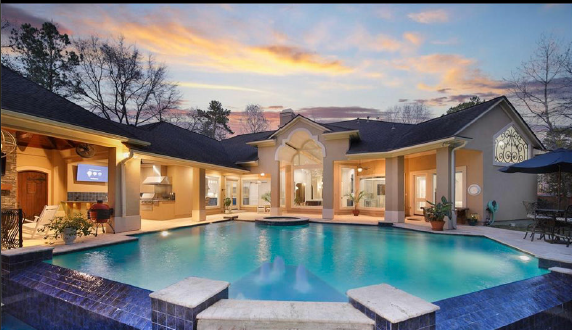 Luxurious backyard pool at dusk with modern home, lit patio, and calm blue water