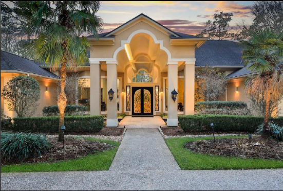 Elegant stucco house entrance with arched doorway, warm lights, and landscaped front walkway at dusk