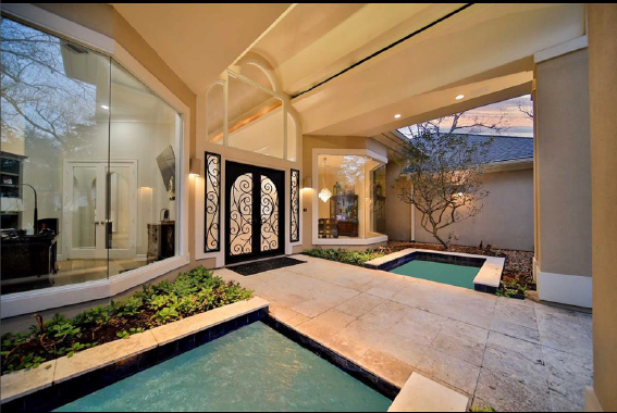 Covered luxury patio with hot tub, cream stone floors, and glass doors at dusk