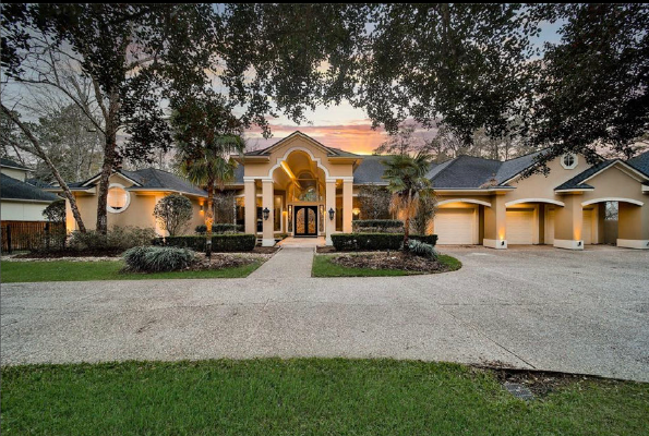 Large suburban house with a lit front entrance, driveway, and trees at dusk