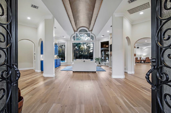 Bright modern entry hall with wood floors, white columns, and ornate black iron gates