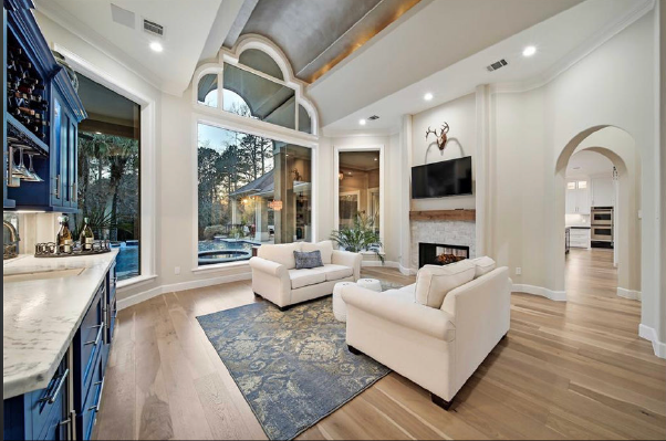 Bright modern living room with white sofas, blue rug, tall windows, and vaulted ceiling
