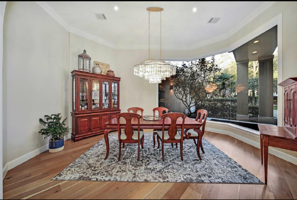 Elegant dining room with wooden table, chairs, chandelier, china cabinet, and large window seat