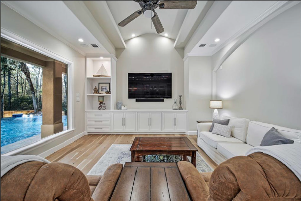 Bright modern living room with white sofa, TV wall, wood coffee table, and pool view through open doors