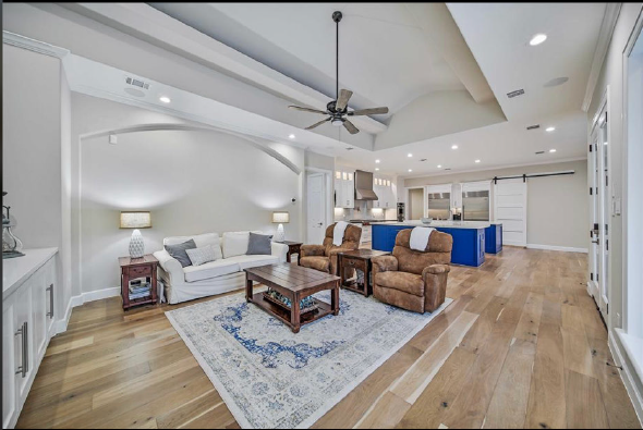 Bright open-concept living room with gray sofa, blue chairs, and kitchen island under vaulted ceilings
