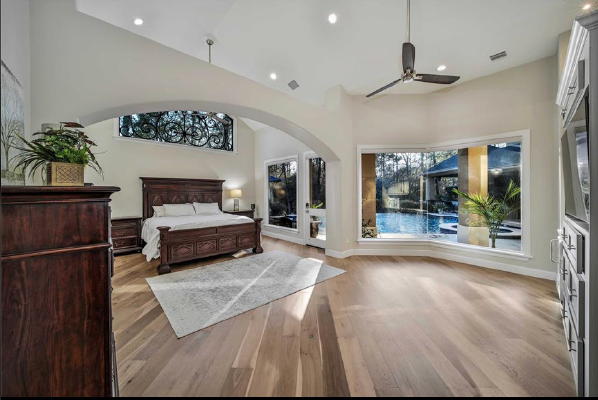 Bright bedroom with a wood bed, vaulted ceiling, and large window view of a pool and garden.