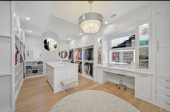 Bright white walk-in closet with built-in shelves, drawers, and a chandelier over a round rug.