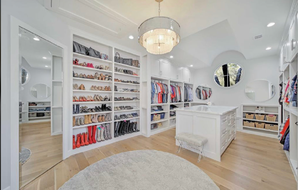 Bright white walk-in closet with shelves of shoes and clothes, a central island, round mirror, and wood floor