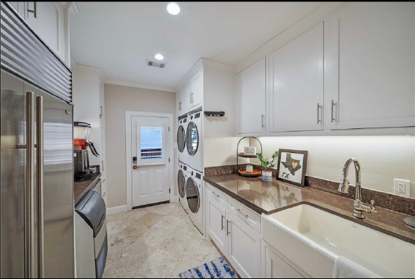Bright galley kitchen with white cabinets, stainless appliances, brown counters, and a washer/dryer at the end.
