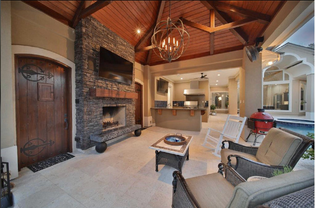 Spacious living room with stone fireplace, vaulted wood ceiling, and kitchen view in the background