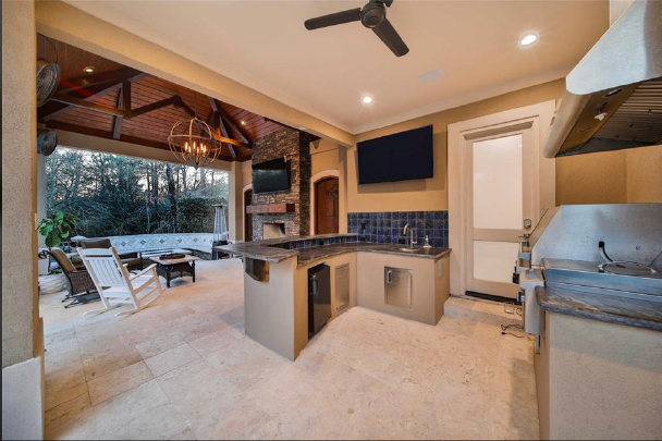 Modern outdoor kitchen with stone counters, grill, bar seating, and open patio facing a backyard pool