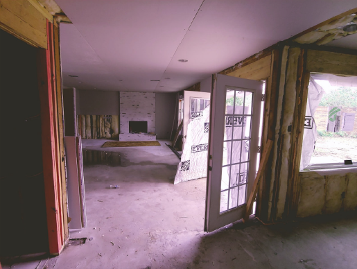 Abandoned room with peeling walls, open door, and dusty floor, viewed toward a second room and fireplace.