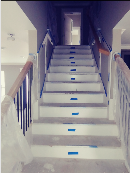 Indoor staircase with white steps, wooden handrails, and blue tape markers leading to a doorway.