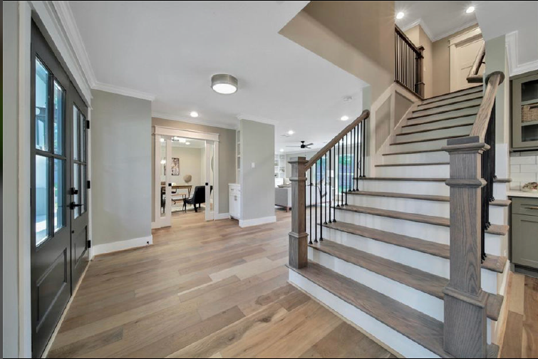 Bright foyer with hardwood floors, staircase, and entry to a dining area in a modern home