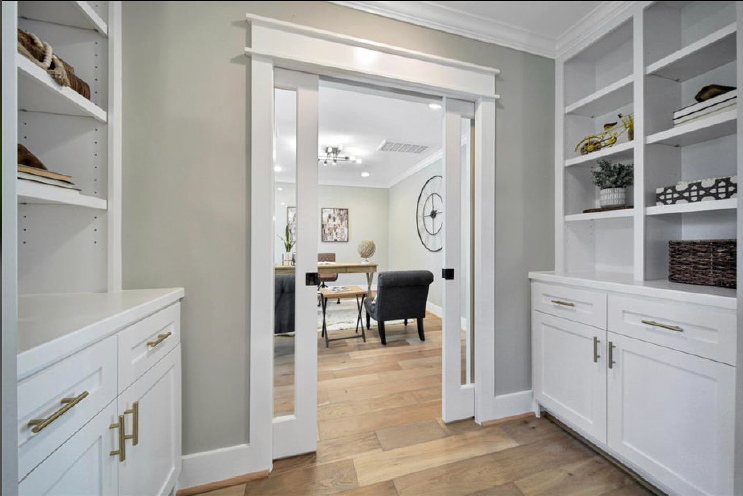 Built-in white shelves and cabinets framing a doorway into a bright dining room with wood floors