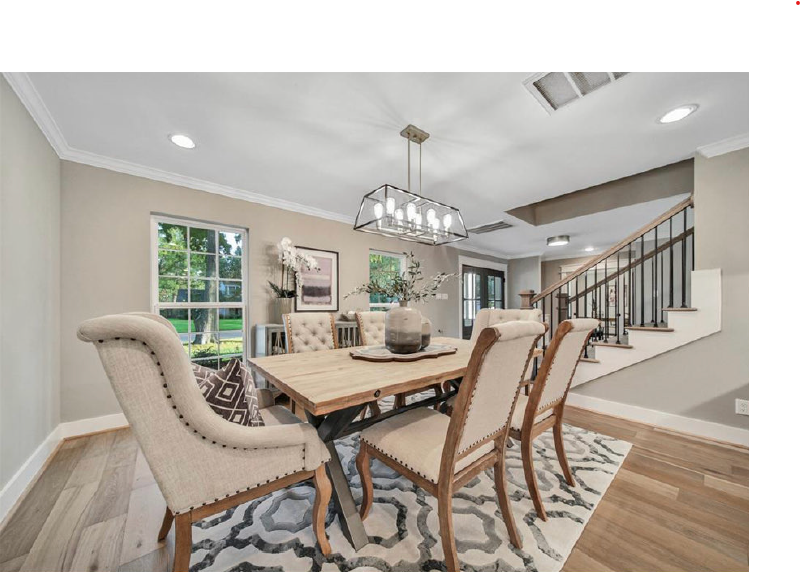 Bright dining room with upholstered chairs, wooden table, chandelier, staircase, and patterned rug