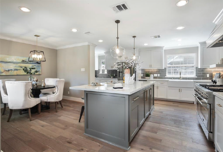 Bright open kitchen and dining area with gray island, white cabinets, wood floors, and chandelier lighting