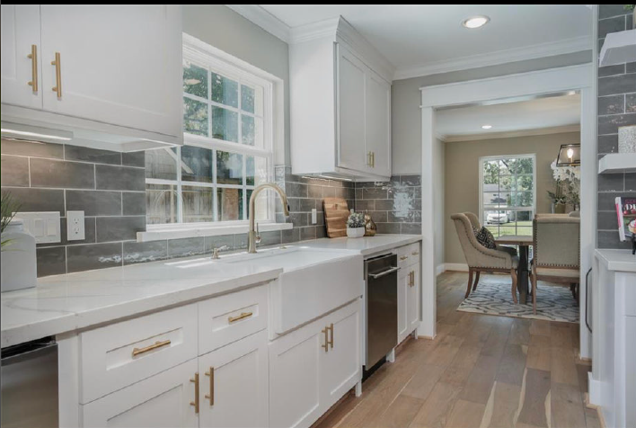 Bright white kitchen with gold hardware, gray tile backsplash, and a view into a dining room