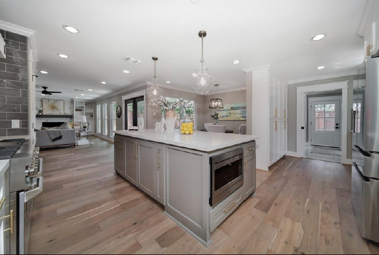 Bright modern kitchen with large island, gray cabinetry, wood floors, and pendant lights