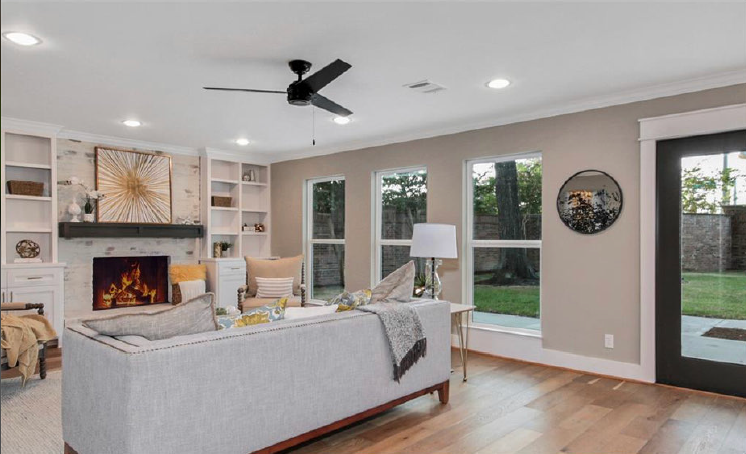 Bright living room with fireplace, built-in shelves, gray sofa, and glass doors to a patio.
