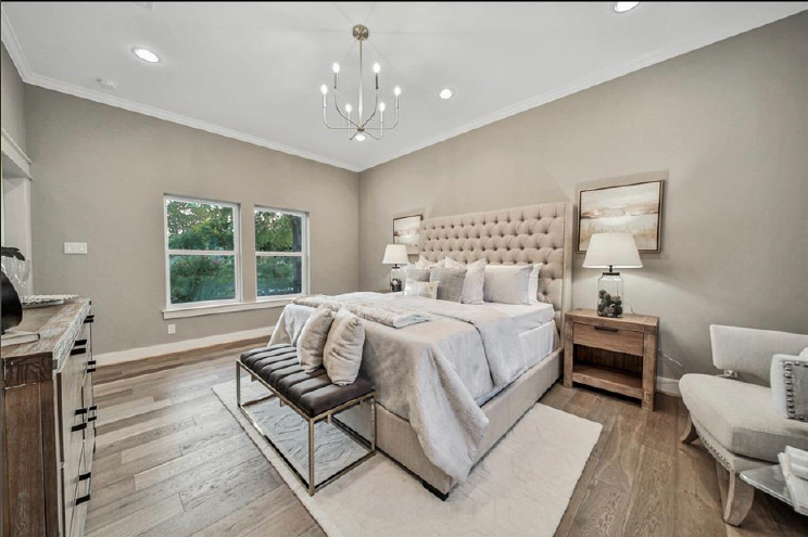 Elegant bedroom with tufted bed, neutral decor, chandelier, and large window with greenery outside