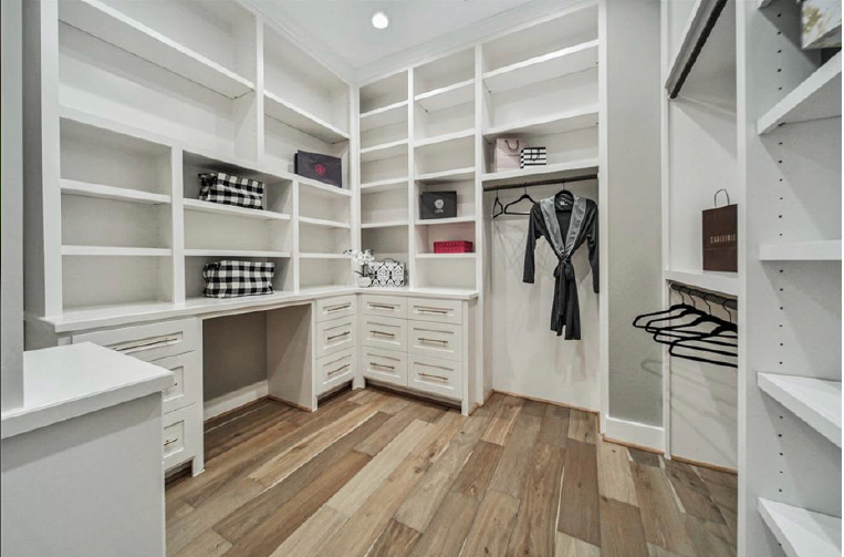 Bright white walk-in closet with built-in shelves, drawers, hanging space, and wood floors
