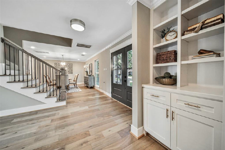 Bright foyer with staircase, built-in shelves, hardwood floors, and black double front doors.
