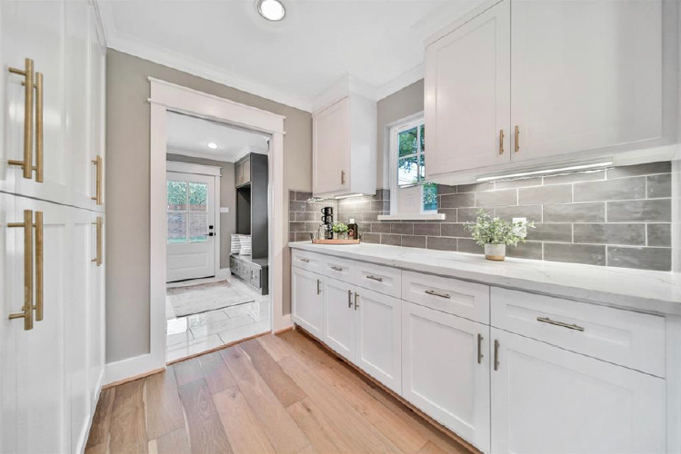 Bright modern kitchen with white cabinets, brass handles, gray tile backsplash, and wood floors