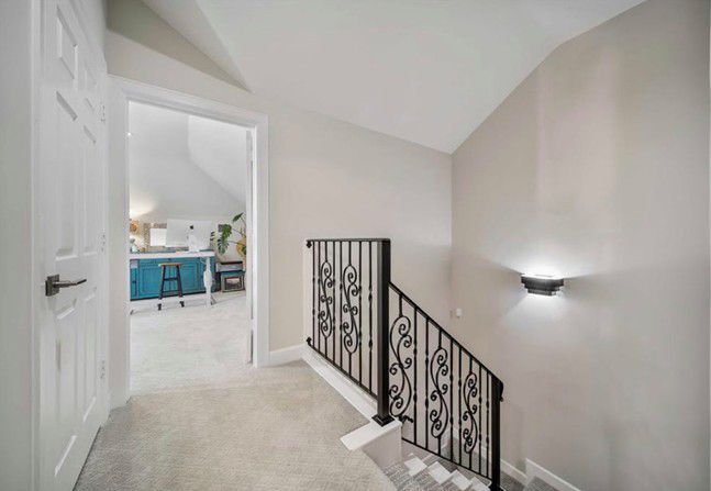 Bright upstairs hallway with white walls, carpet, stair railing, and a view into a blue-accented room
