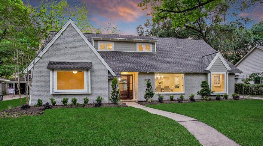 Gray suburban house with lit windows, manicured lawn, and curved walkway at dusk Gray suburban house with lit windows, manicured lawn, and curved walkway at dusk