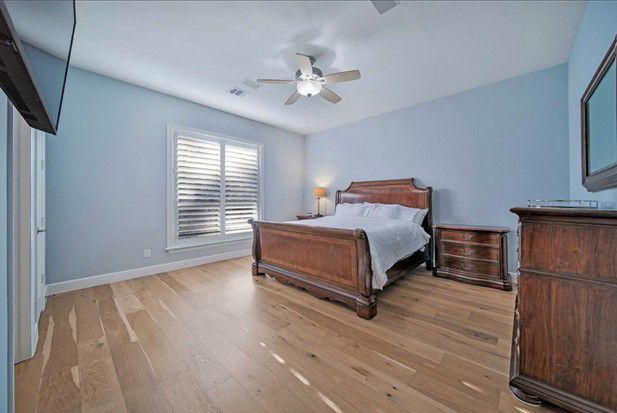 Spacious light-blue bedroom with wooden bed, dresser, nightstands, and shuttered window Spacious light-blue bedroom with wooden bed, dresser, nightstands, and shuttered window