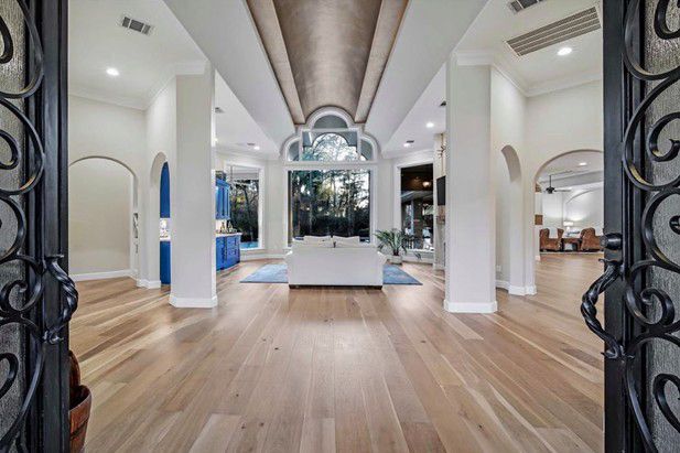 Elegant white showroom with wood floors, arched doorways, and ornate black gates at the entrance