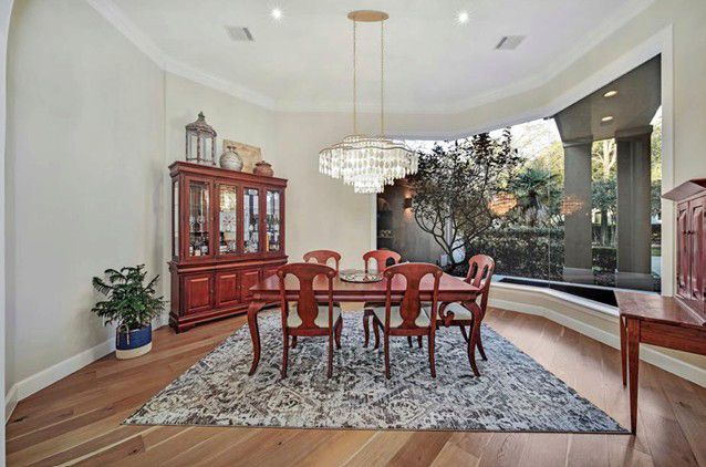 Elegant dining room with a wooden table, red chairs, chandelier, and a large curved window overlooking greenery