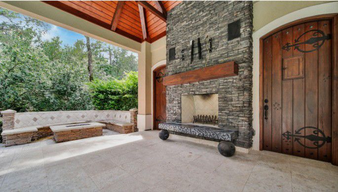 Covered stone patio with outdoor fireplace, wooden door, and bench seating