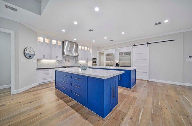 Bright modern kitchen with blue island cabinets, white countertops, hardwood floors, and stainless steel appliances