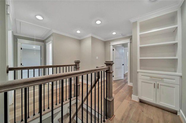 Bright hallway with hardwood floors, white walls, built-in shelves, and black stair railing.