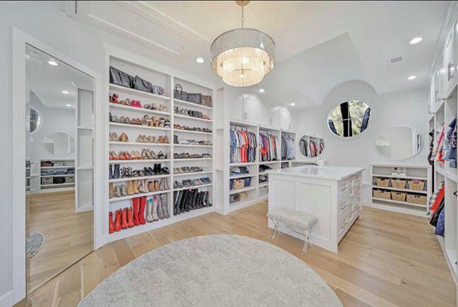Bright white walk-in closet with shelves of shoes, hanging clothes, a central island, and round mirror