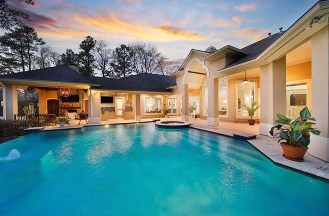 Luxury backyard pool at dusk beside a modern house, with warm lights and a colorful sunset sky.