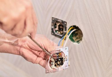 Hands wiring an electrical outlet box in a wall opening
