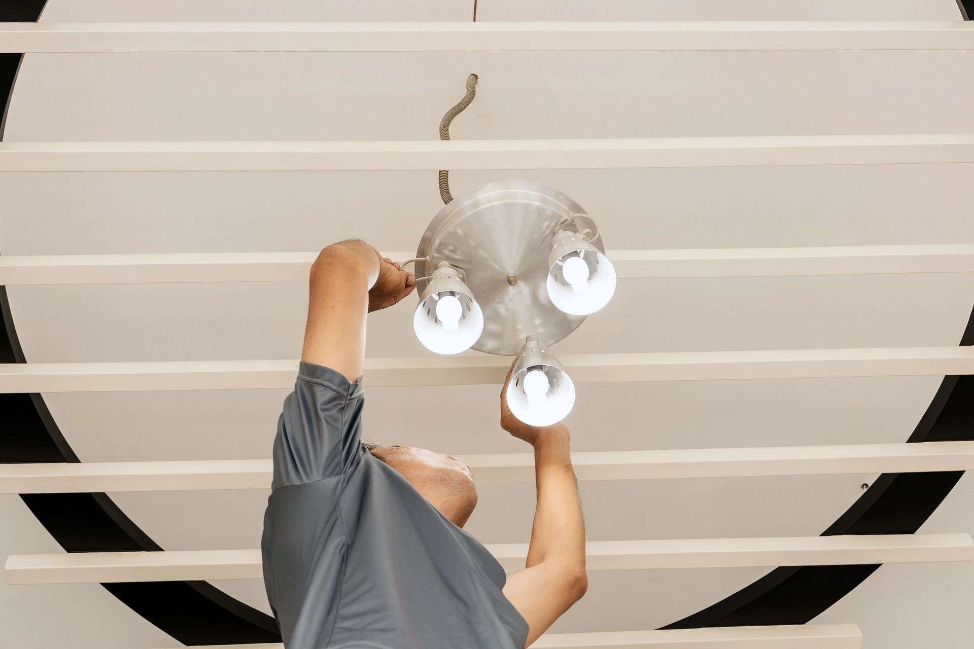 Person changing a ceiling light fixture with a screwdriver in a white room