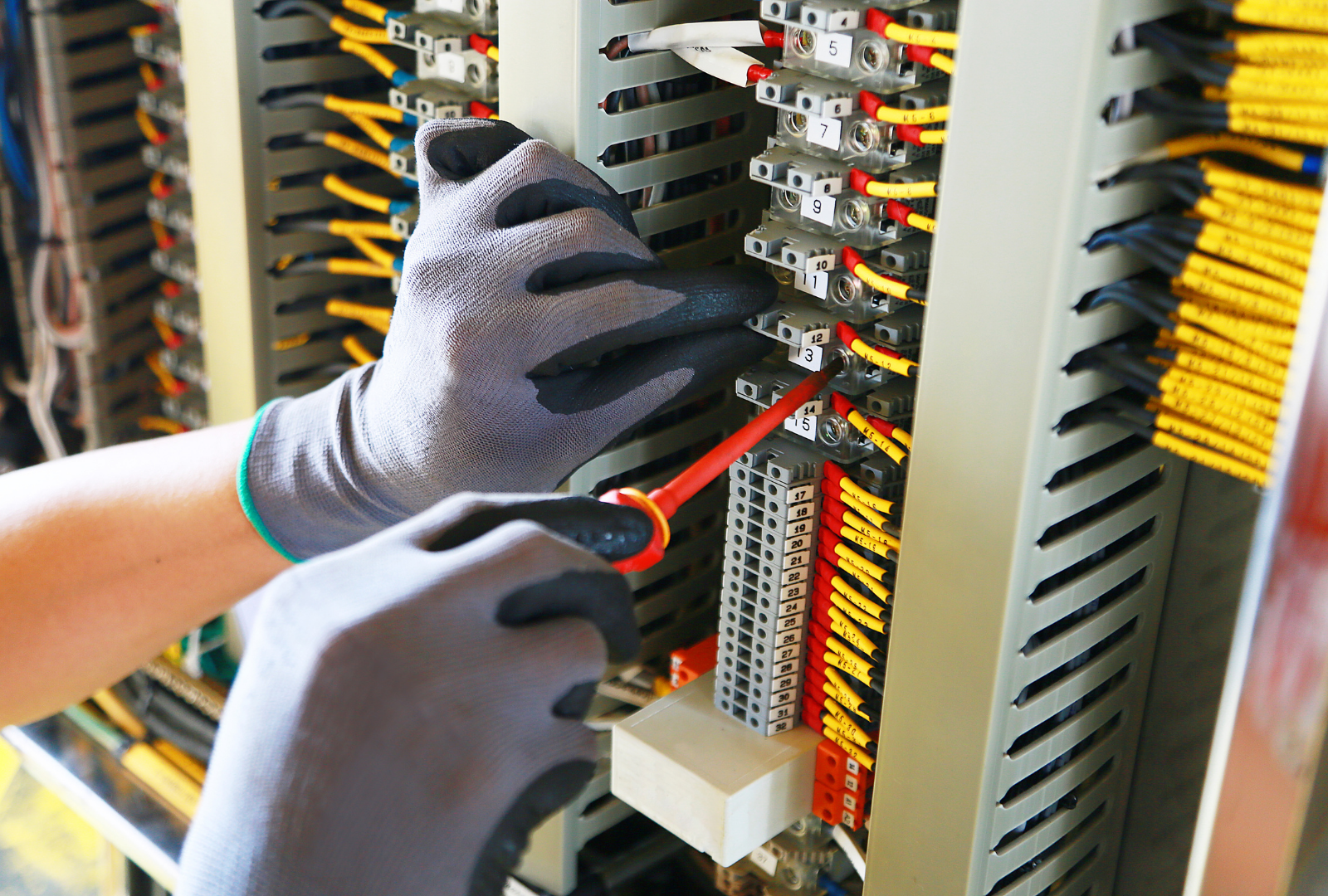 Gloved hands adjusting wiring inside an electrical control panel with red and black cables