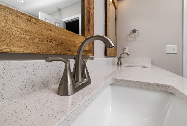 Bathroom sink with chrome faucet, speckled white countertop, and wood-framed mirror