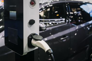 Electric car charging at a station beside a dark vehicle at night