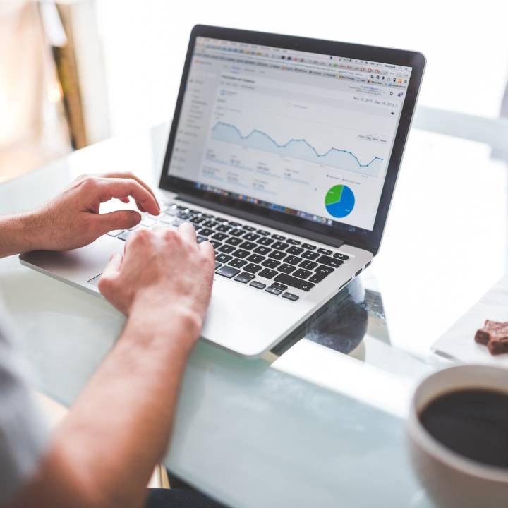 Hands typing on a laptop showing analytics charts at a bright desk, with a coffee cup nearby