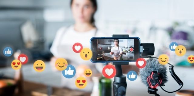 Person livestreaming on a smartphone with social media reaction icons floating around a blurred background
