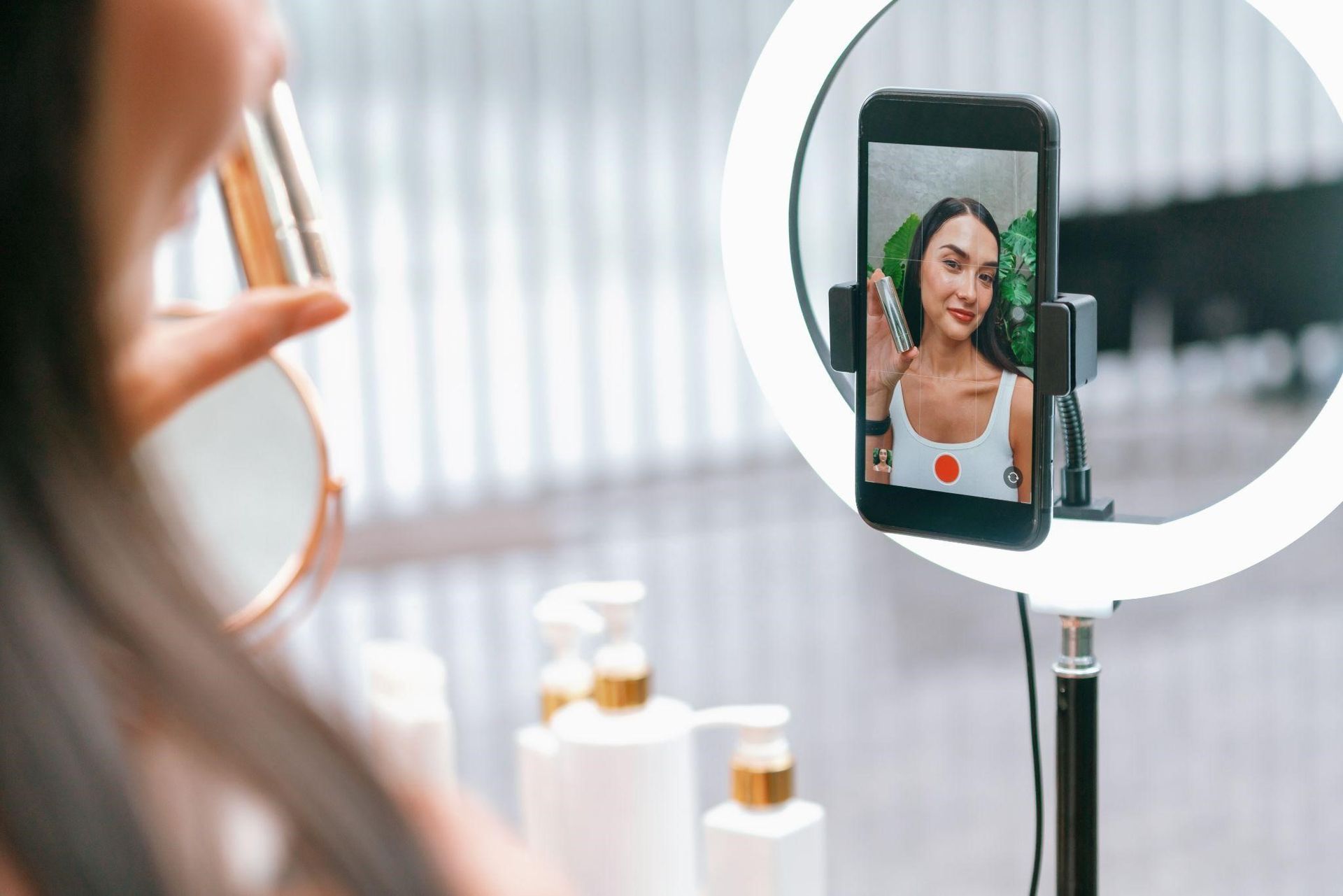 Smartphone on a ring light shows a woman recording a video selfie in a bright room