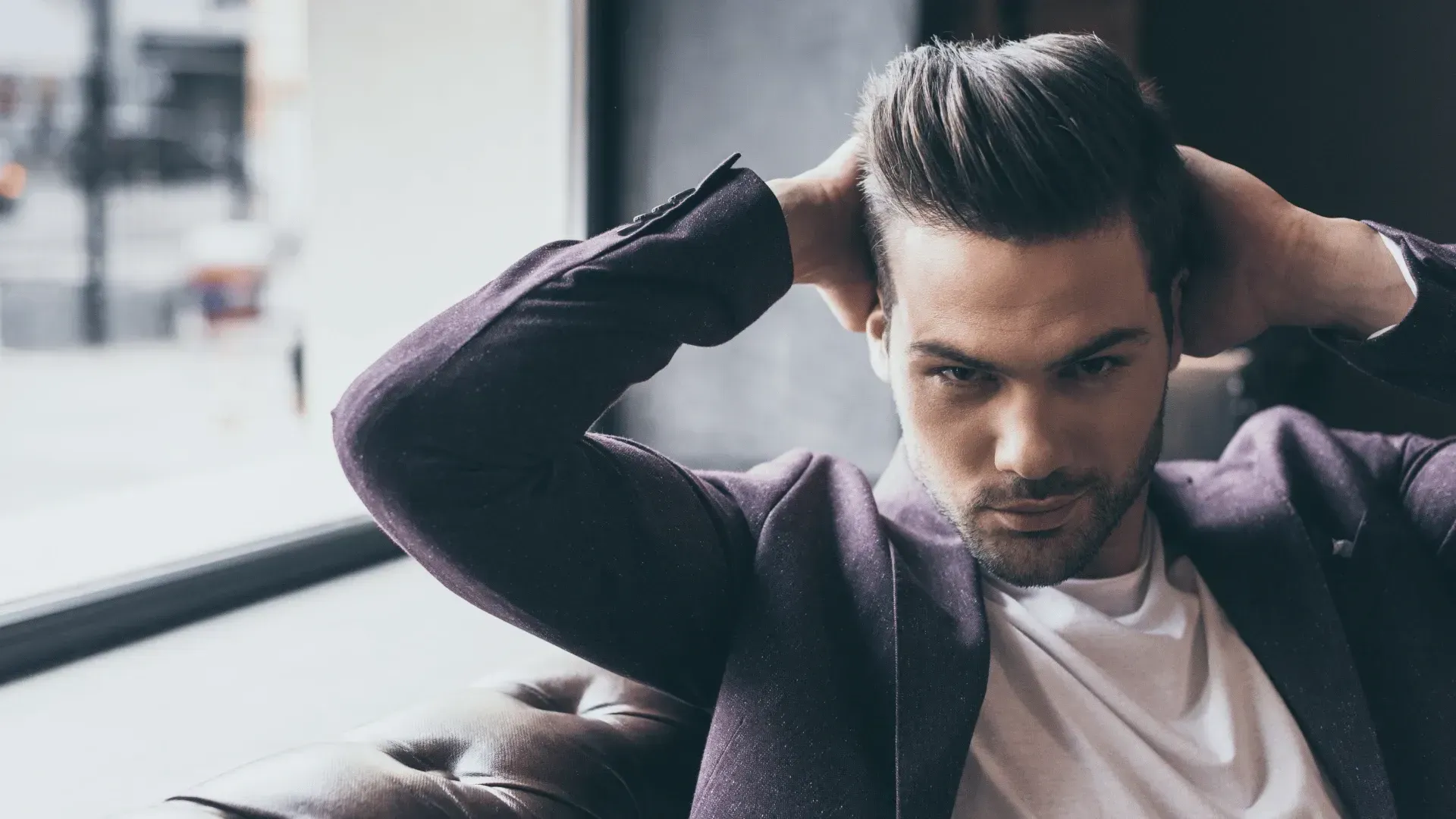 A man in a suit is sitting on a couch with his hands in his hair.