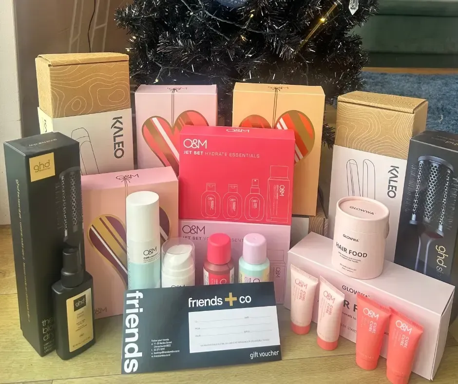 Assorted beauty and hair product gift sets and a voucher near a tree.